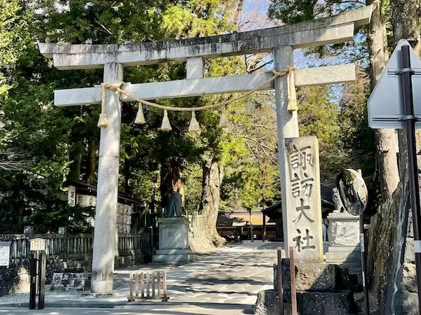 The stone torii gate at Suwa Taisha Harumiya, marking the entrance to the sacred shrine grounds.